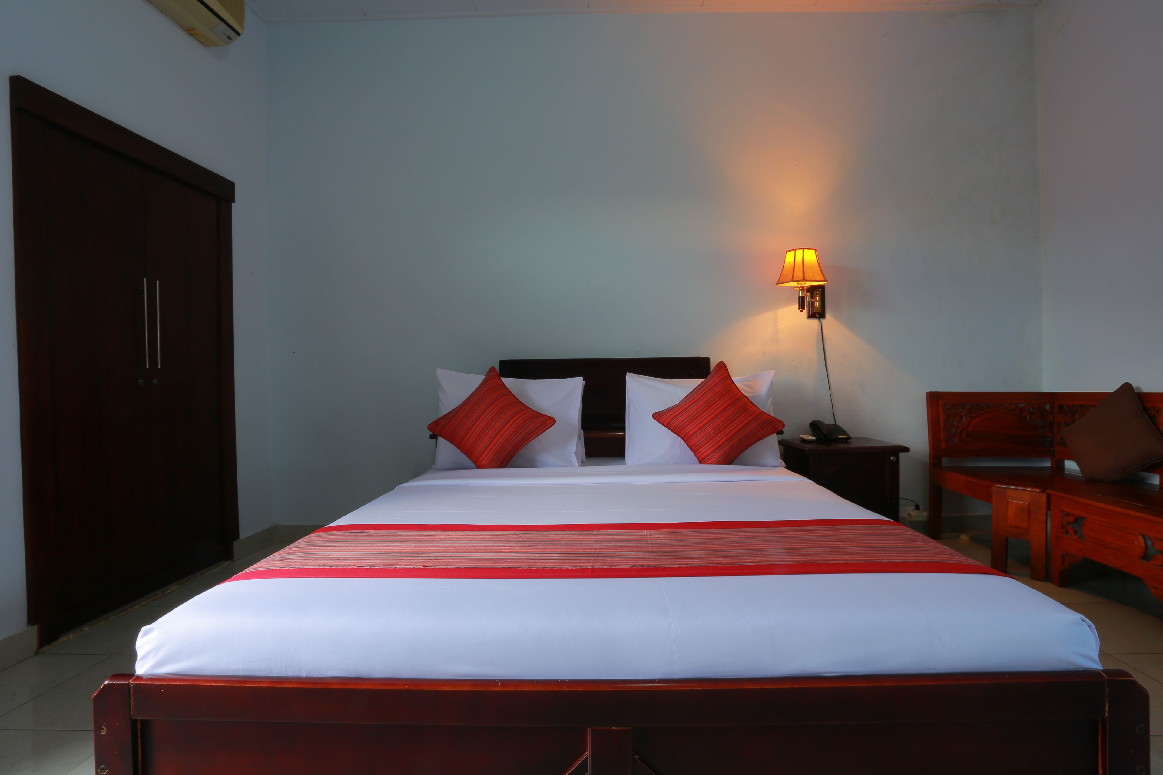 A neatly made bed with a red-striped bedspread, a bedside lamp, and a wooden nightstand.