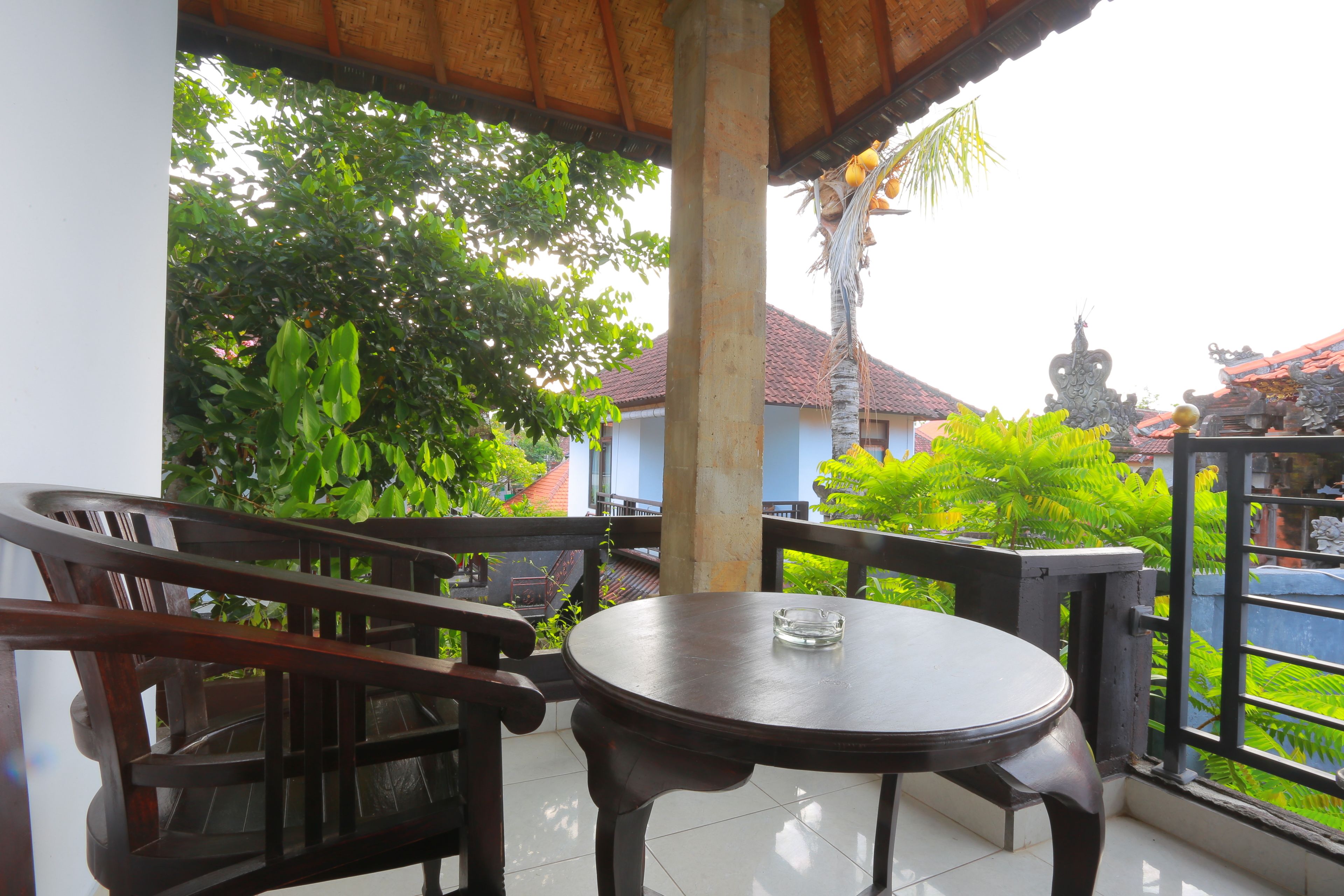 A wooden table and chair set on a balcony with a view of a garden and buildings.