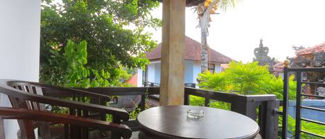 A wooden table and chair set on a balcony with a view of a garden and buildings.
