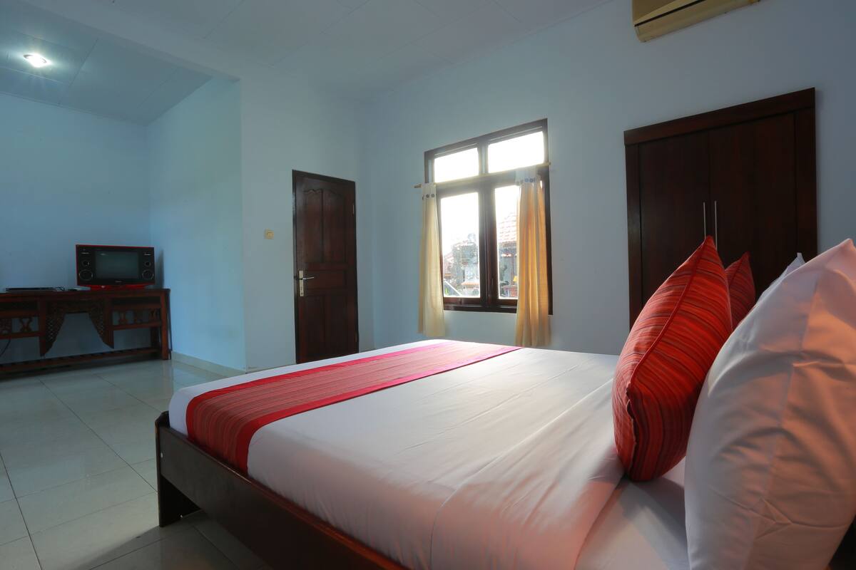 A bedroom with a bed, a television on a wooden cabinet, and a window with curtains.