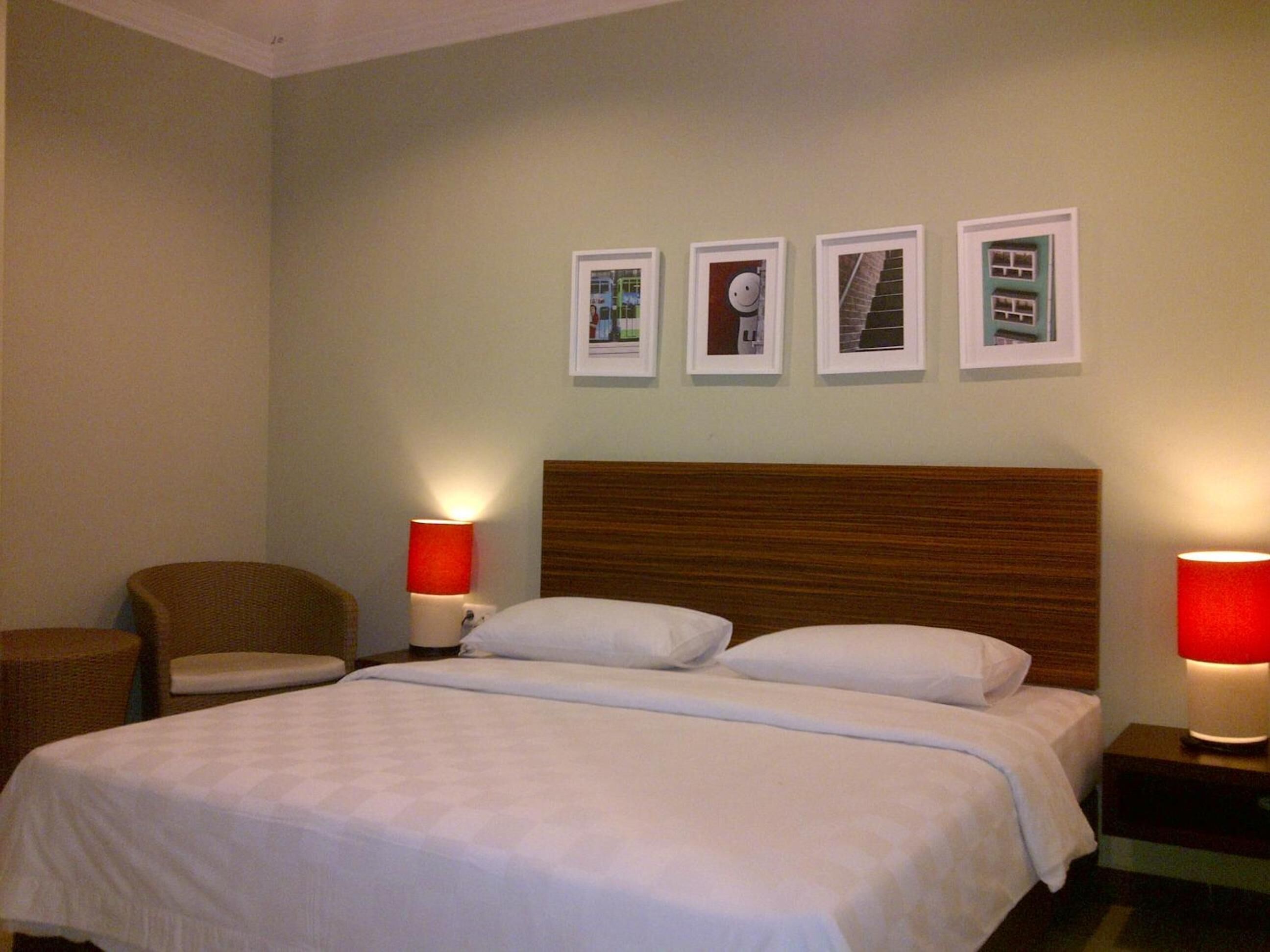 Quarto de hotel com uma cama grande, duas mesinhas de cabeceira com luminárias, uma cadeira e quatro quadros na parede.