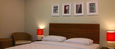 Quarto de hotel com uma cama grande, duas mesinhas de cabeceira com luminárias, uma cadeira e quatro quadros na parede.
