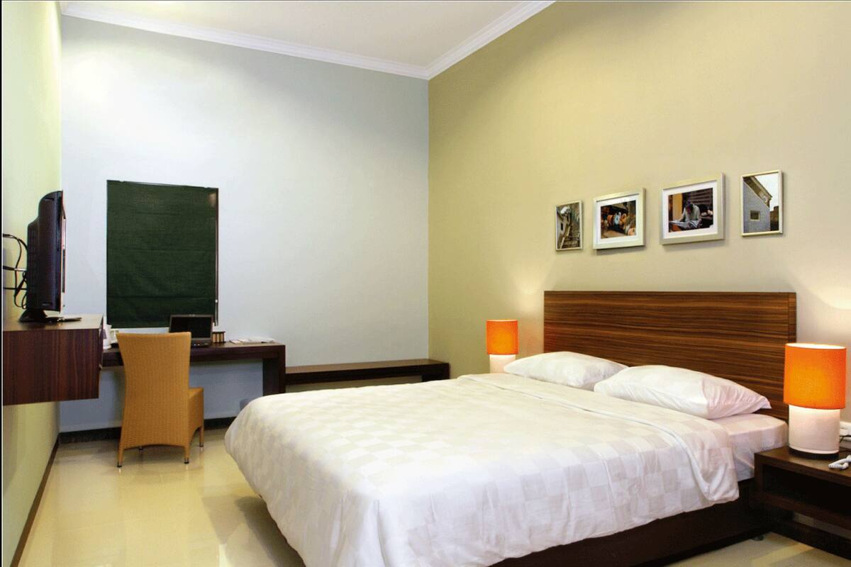 Een hotelkamer met een bed, een bureau met stoel, een televisietoestel en een wand met ingekaderde foto's.