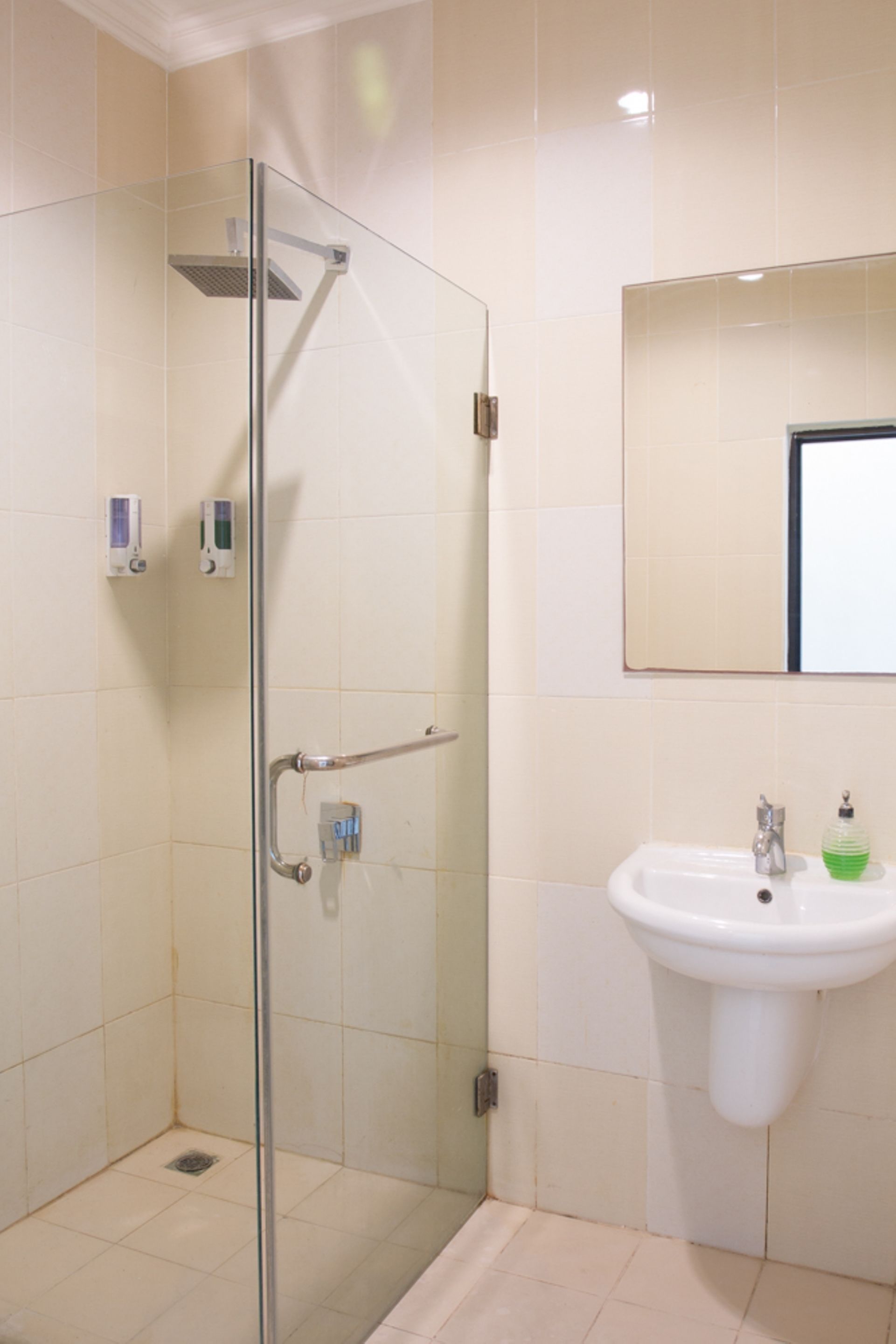 Un baño con mampara de vidrio, un lavamanos con espejo y suelo de baldosas.