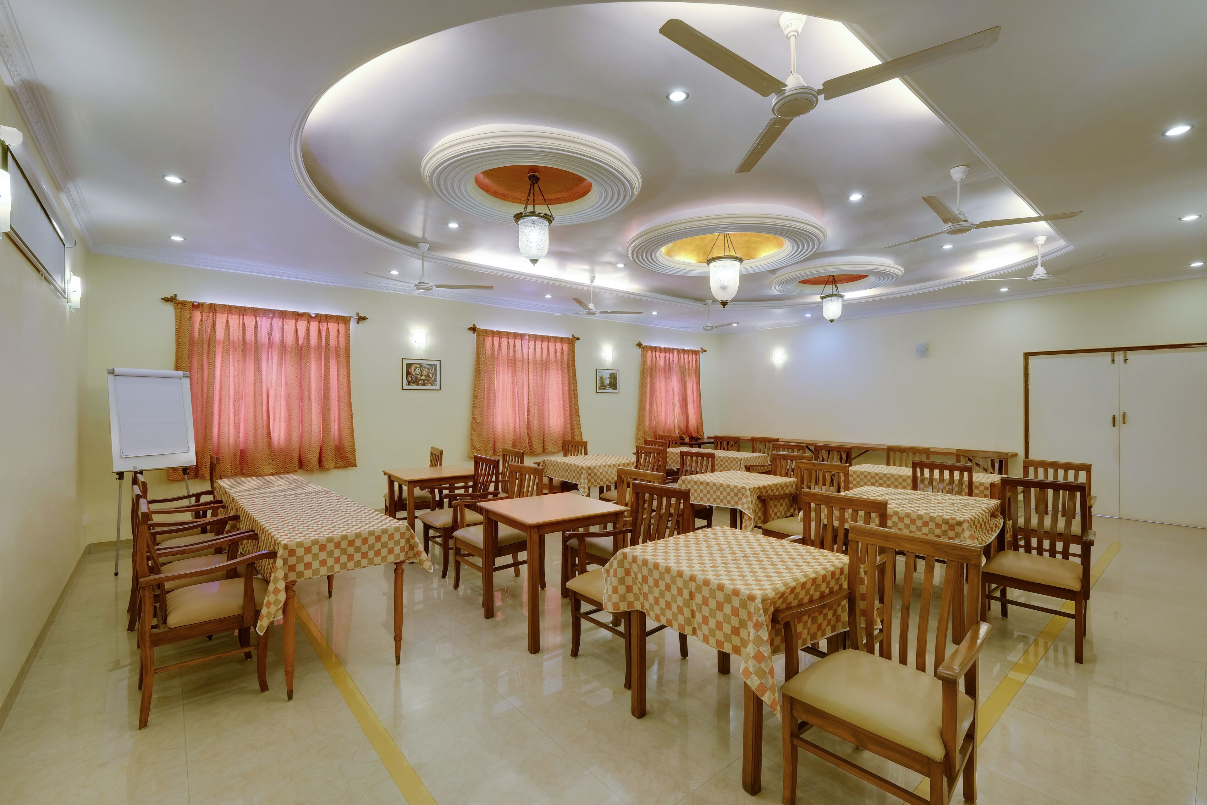 A conference room with multiple tables and chairs, ceiling fans, and recessed lighting.