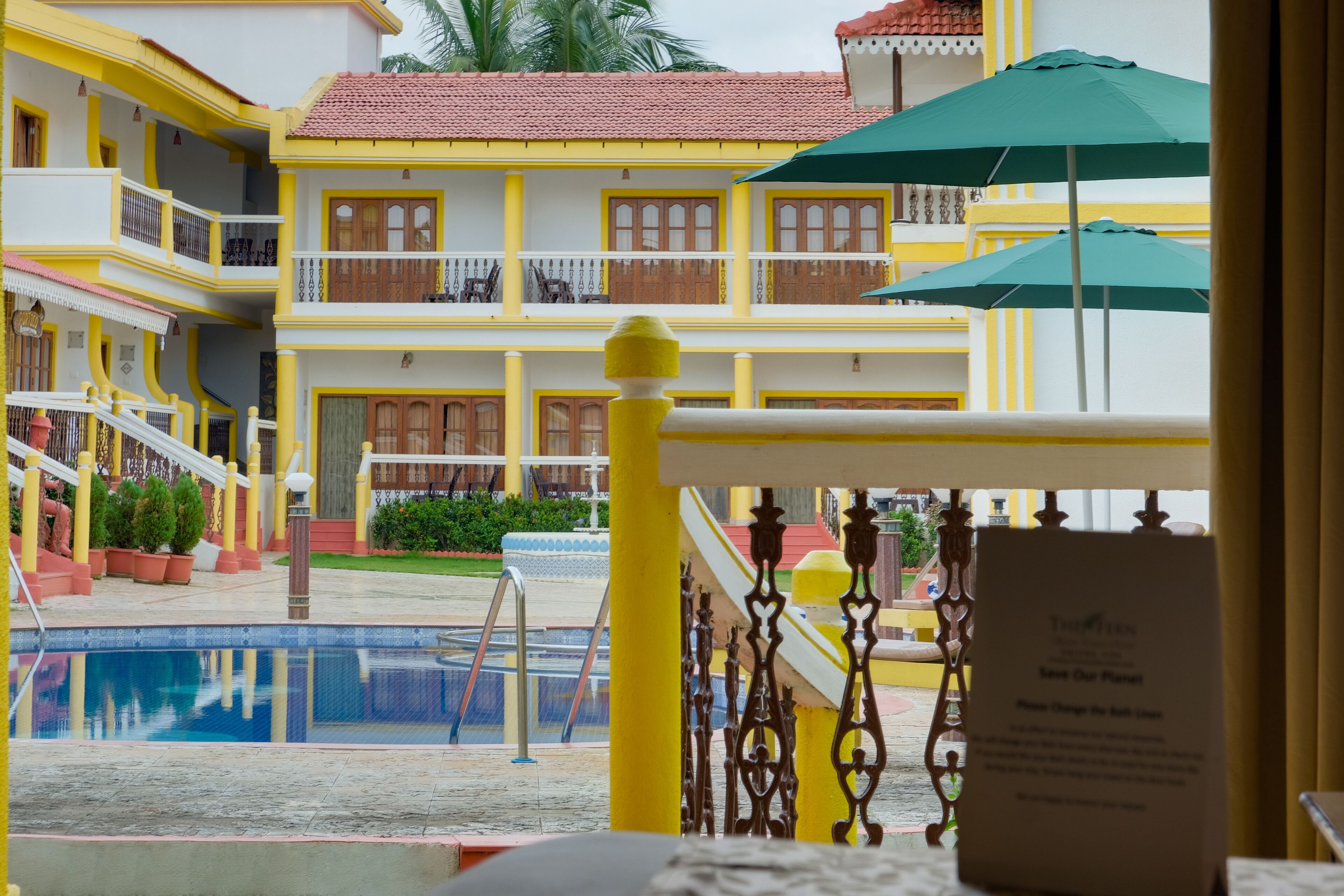 Un hotel con piscina, fachada amarilla y blanca, balcones y un cartel que dice "Save Our Planet".