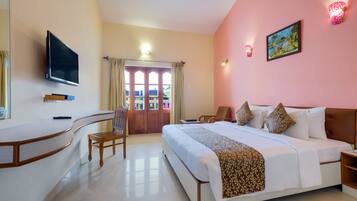 Habitación de hotel con cama, escritorio, silla, televisión y puerta que da a un balcón.