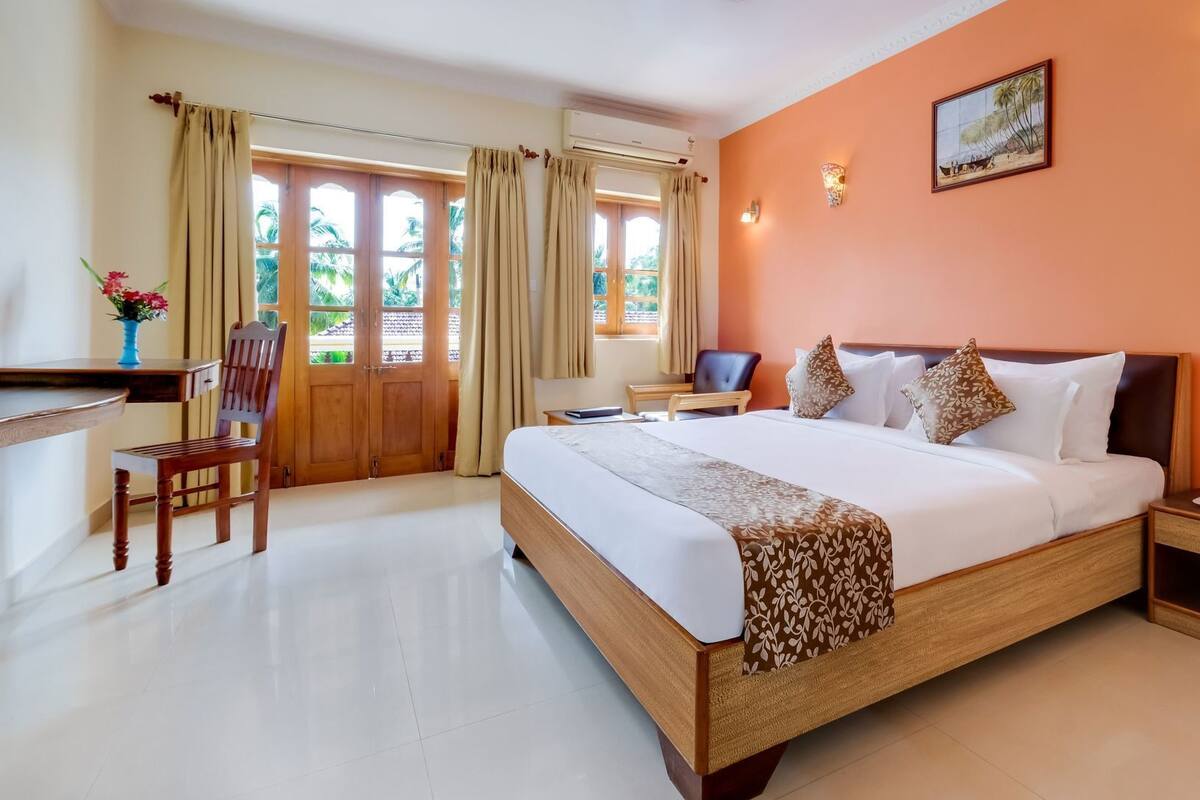 Une chambre d’hôtel avec un lit, un bureau, une chaise, une fenêtre avec des rideaux et un tableau au mur.
