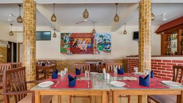 A restaurant with wooden tables and chairs, a mural on the wall, and a bar area.