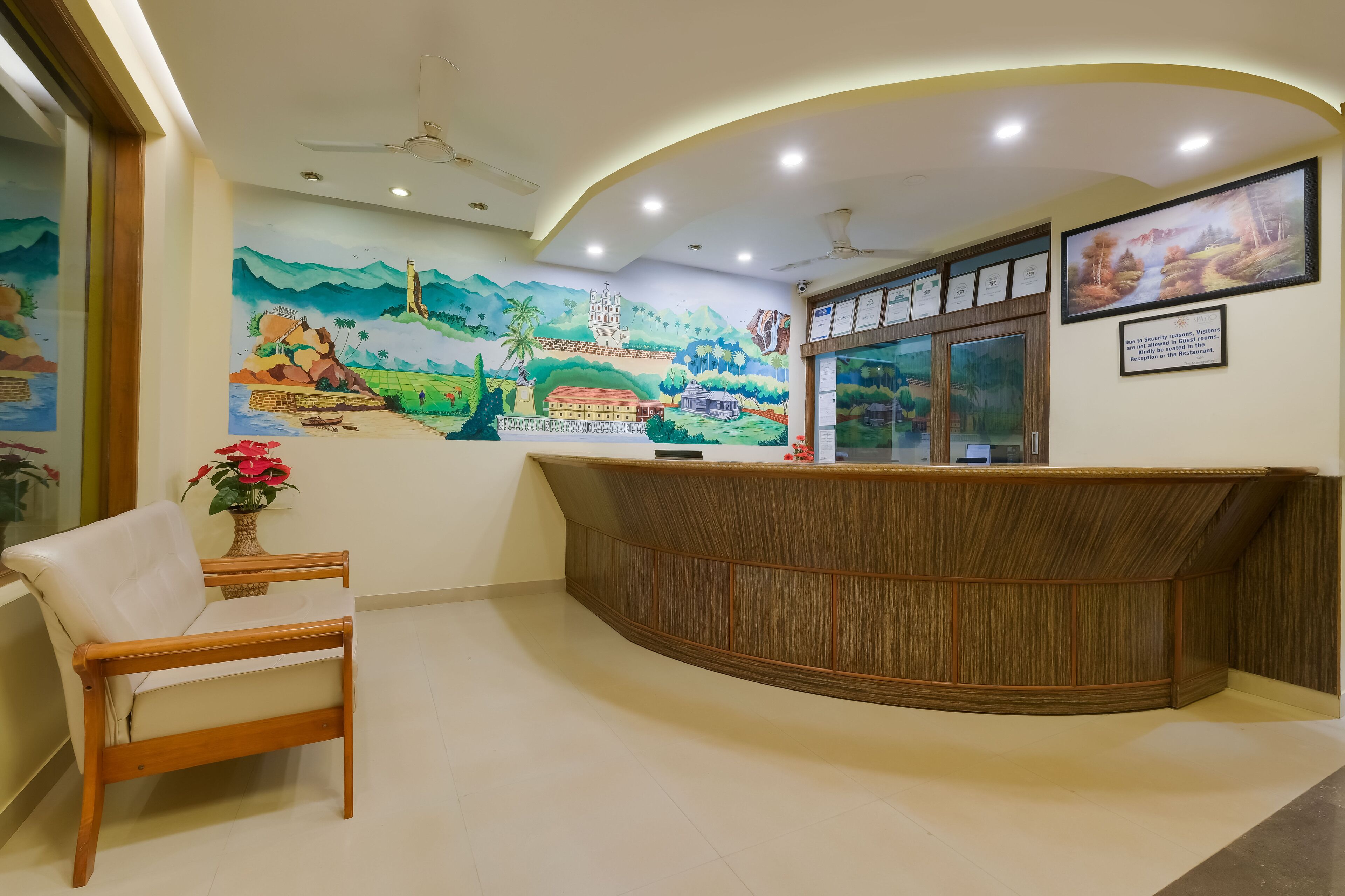 A reception area with a wooden reception desk, a cushioned chair, a wall mural, ceiling lights, and framed certificates.