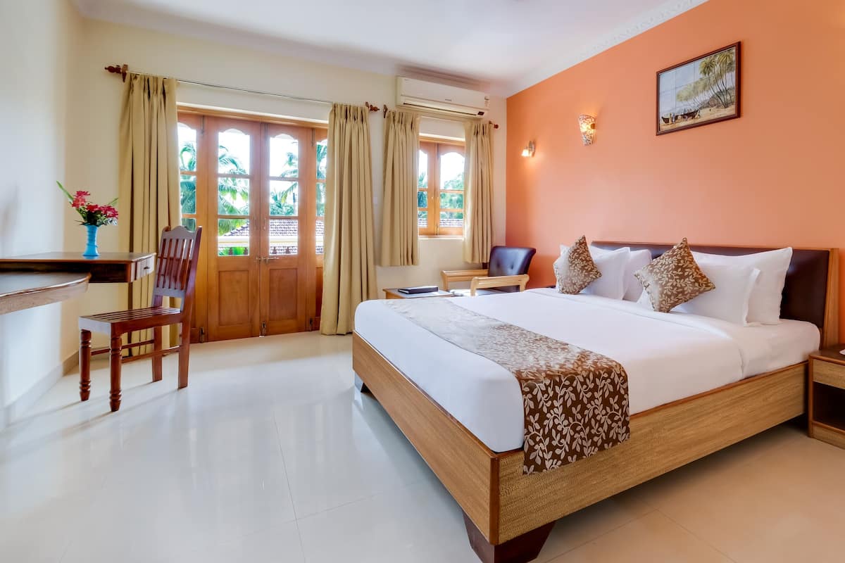 Une chambre d’hôtel avec un grand lit, un bureau avec une chaise et une vue sur les palmiers par la fenêtre.