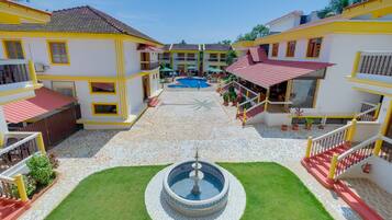 Un patio central con una fuente, rodeado por edificios de varios pisos con balcones y una piscina al fondo.
