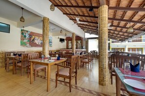 A restaurant with wooden tables and chairs, a tiled floor, and a high ceiling with exposed beams.