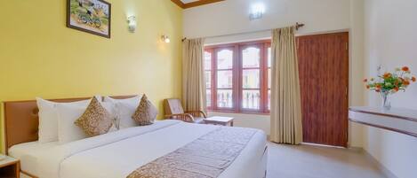 Habitación de hotel con una cama grande, una silla, una mesita, una ventana con cortinas y una lámpara fijada a la pared.