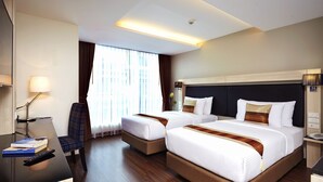 Habitación de hotel con dos camas, un escritorio con lámpara, una silla y un ventanal con cortinas.