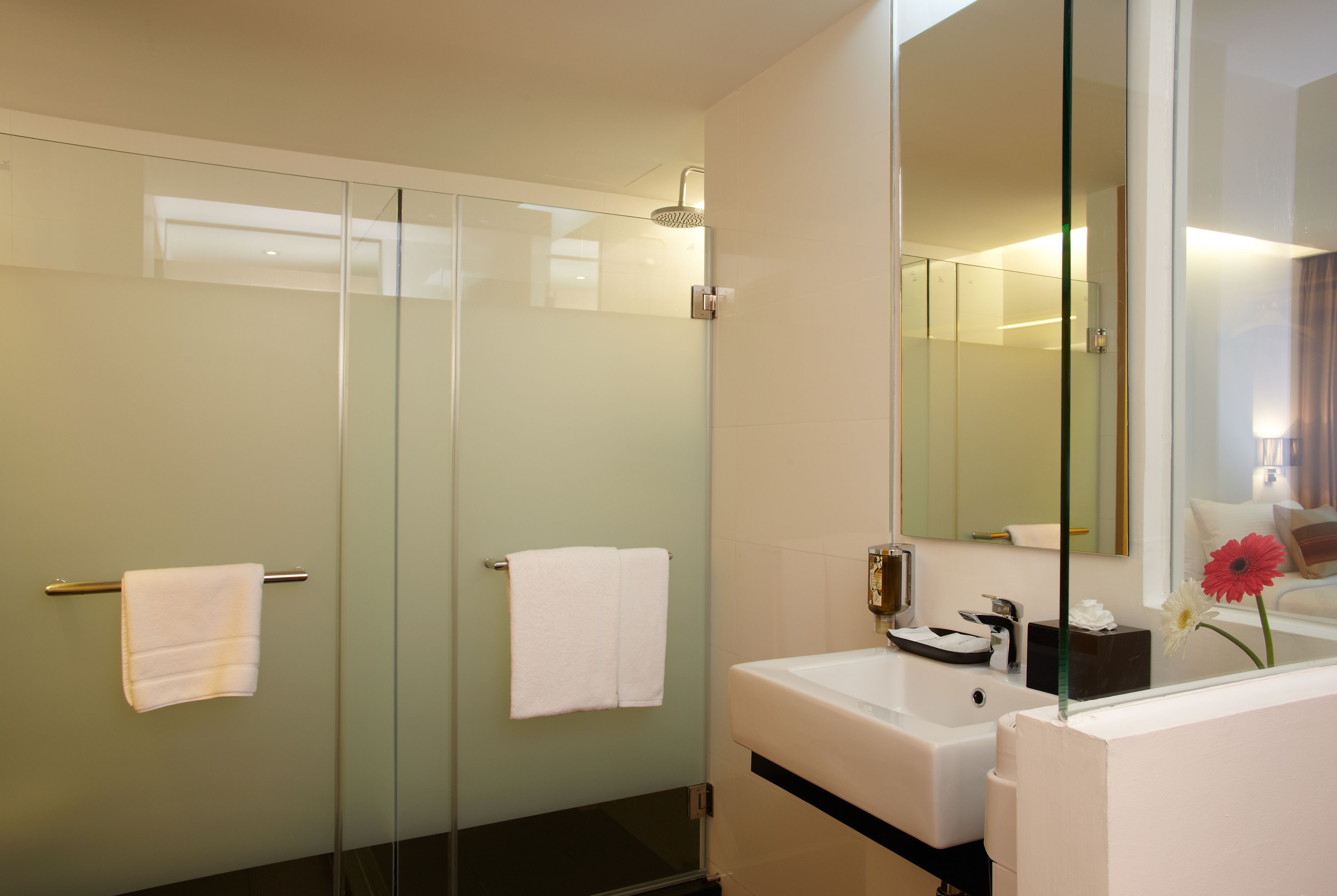 Un bagno moderno con cabina doccia in vetro, un lavandino bianco e uno specchio grande.
