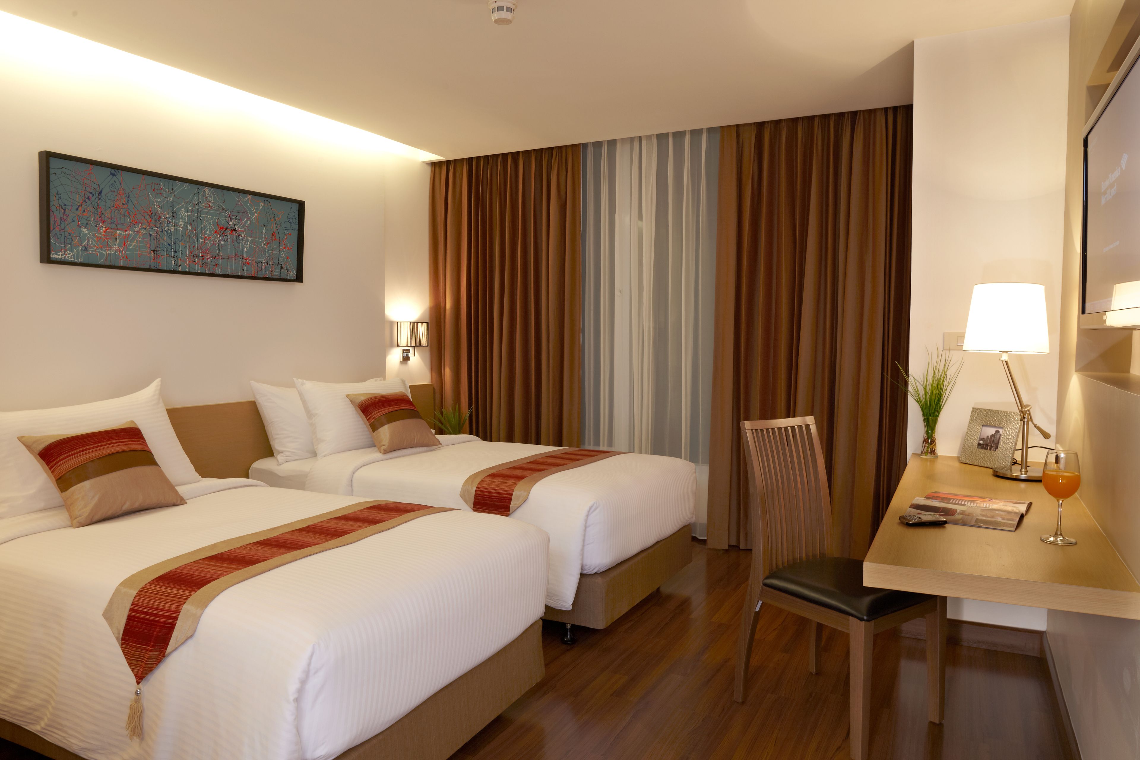 A hotel room with two beds, a desk with a lamp, a chair, and a painting on the wall.