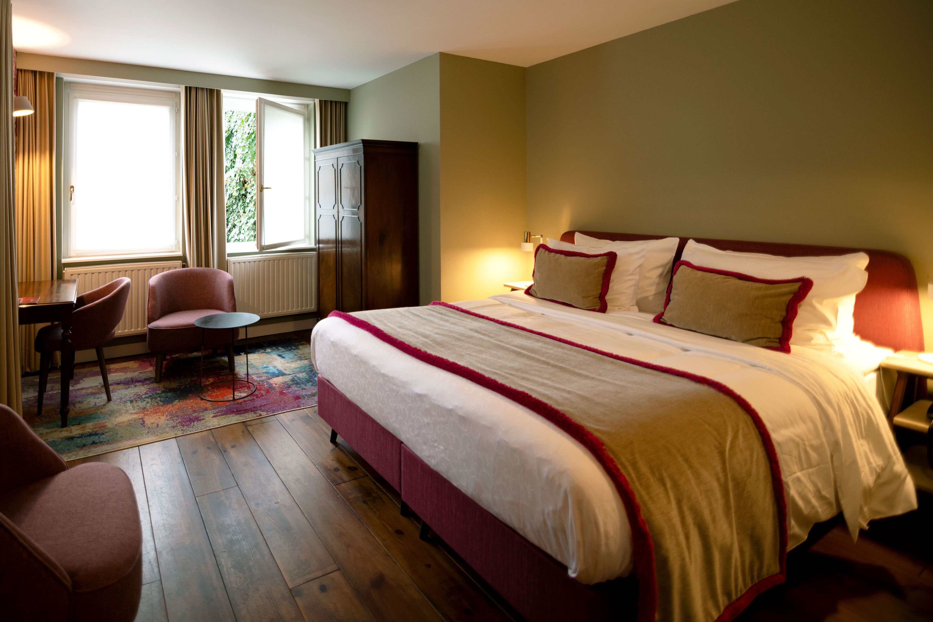 A hotel room with a large bed, a desk, a chair, and a wardrobe.