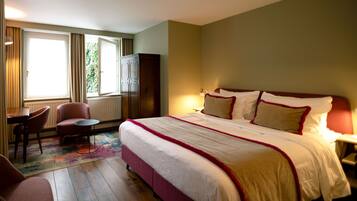 A hotel room with a large bed, a desk, a chair, and a wardrobe.
