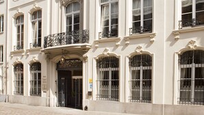 Un edificio histórico con detalles arquitectónicos ornamentales, incluyendo una entrada central con un arco decorativo y varios balcones con barandillas de hierro forjado.