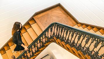A woman descending a wooden staircase with ornate black railings.