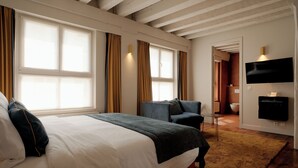 Habitación de hotel con una cama grande, una silla, un televisor y un baño visible a través de una puerta abierta.