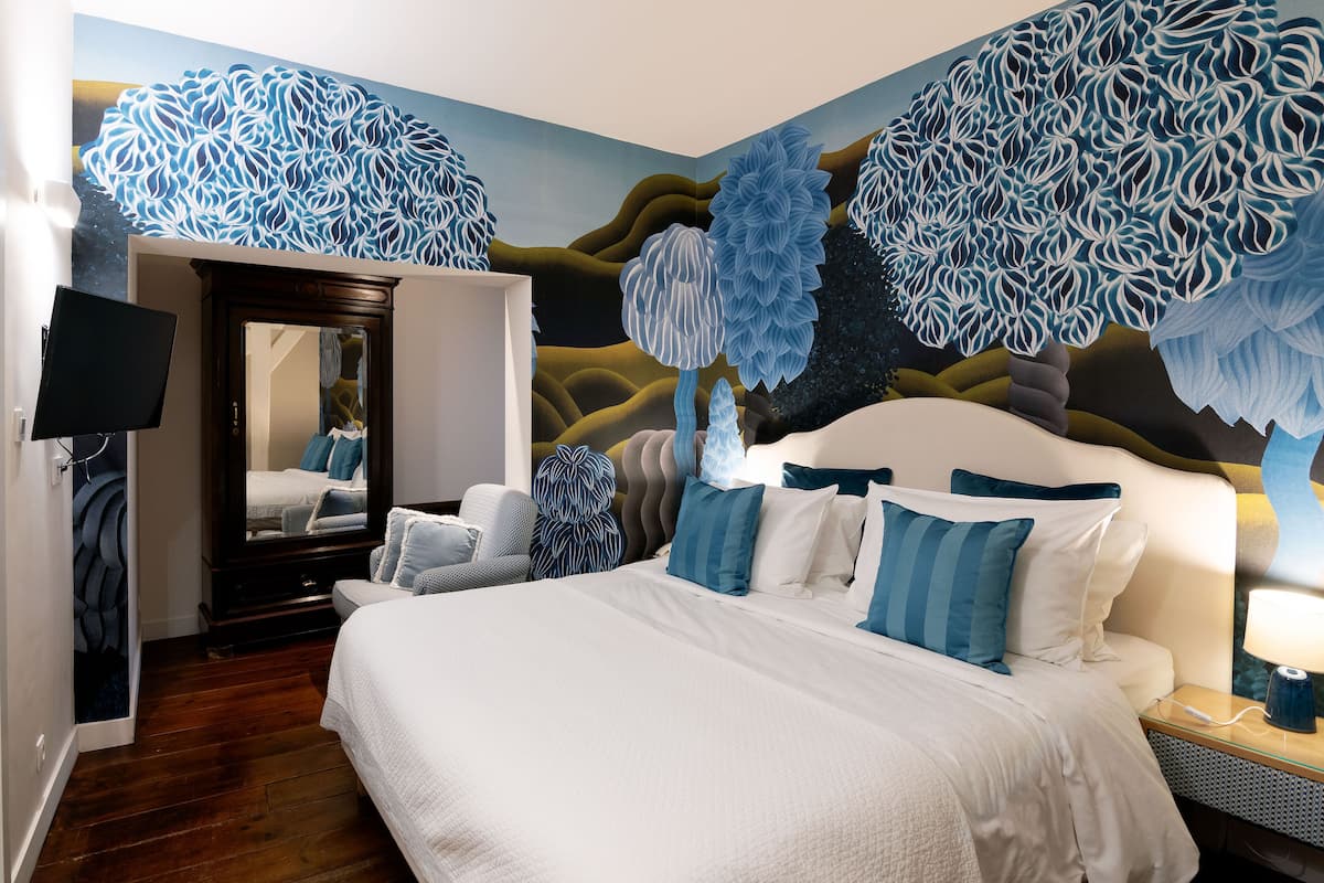 A hotel room with a large bed, a flat-screen TV, a mirror, and a wall mural.