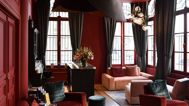 Una habitación con una pared roja, un armario negro, un sofá color crema y un sillón rojo.
