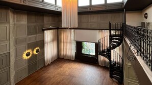 Una habitación amplia con piso de madera, un gran candelabro, una escalera en espiral y vistas a través de una ventana.