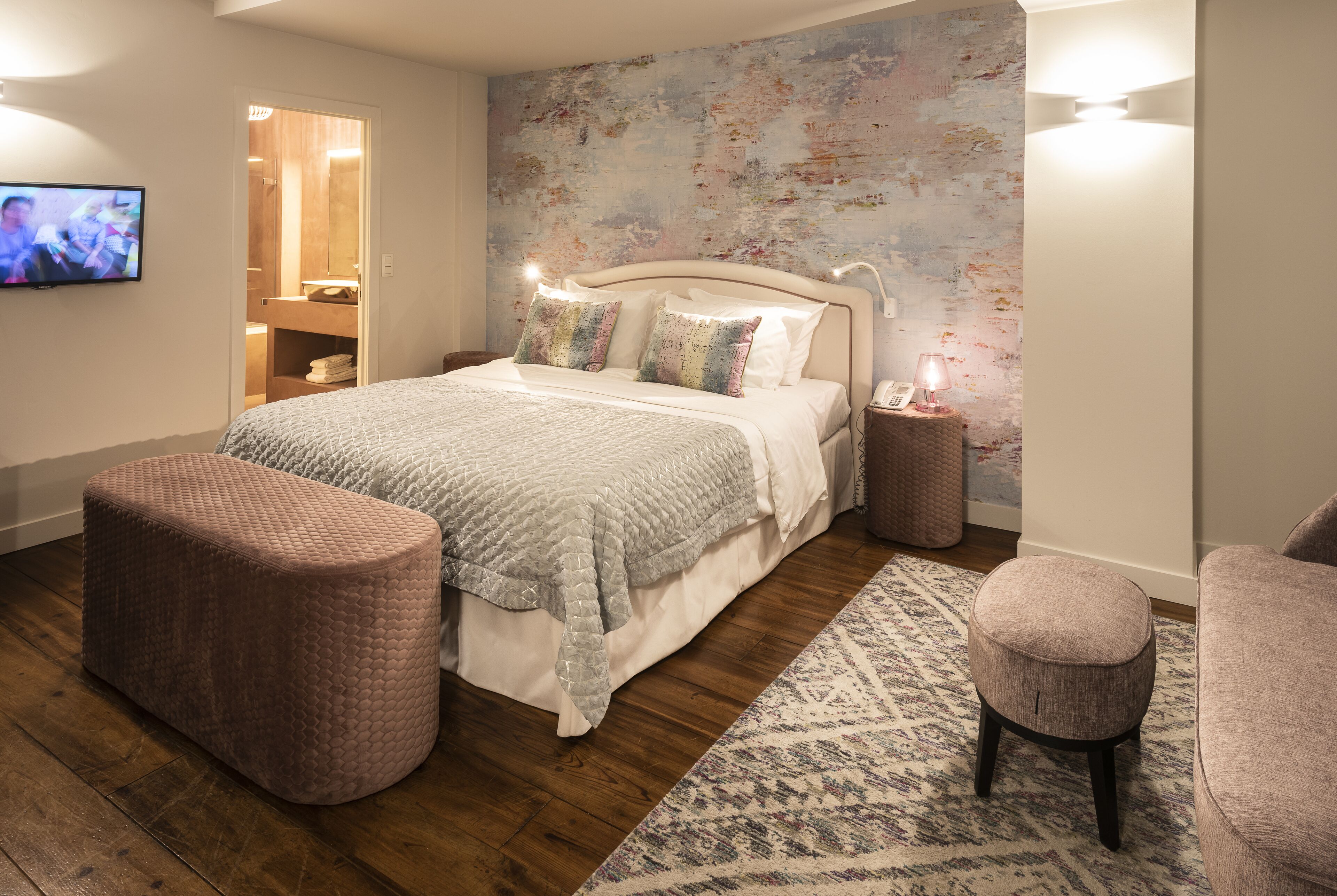A modern bedroom with a large bed, two ottomans, a nightstand, and a TV.