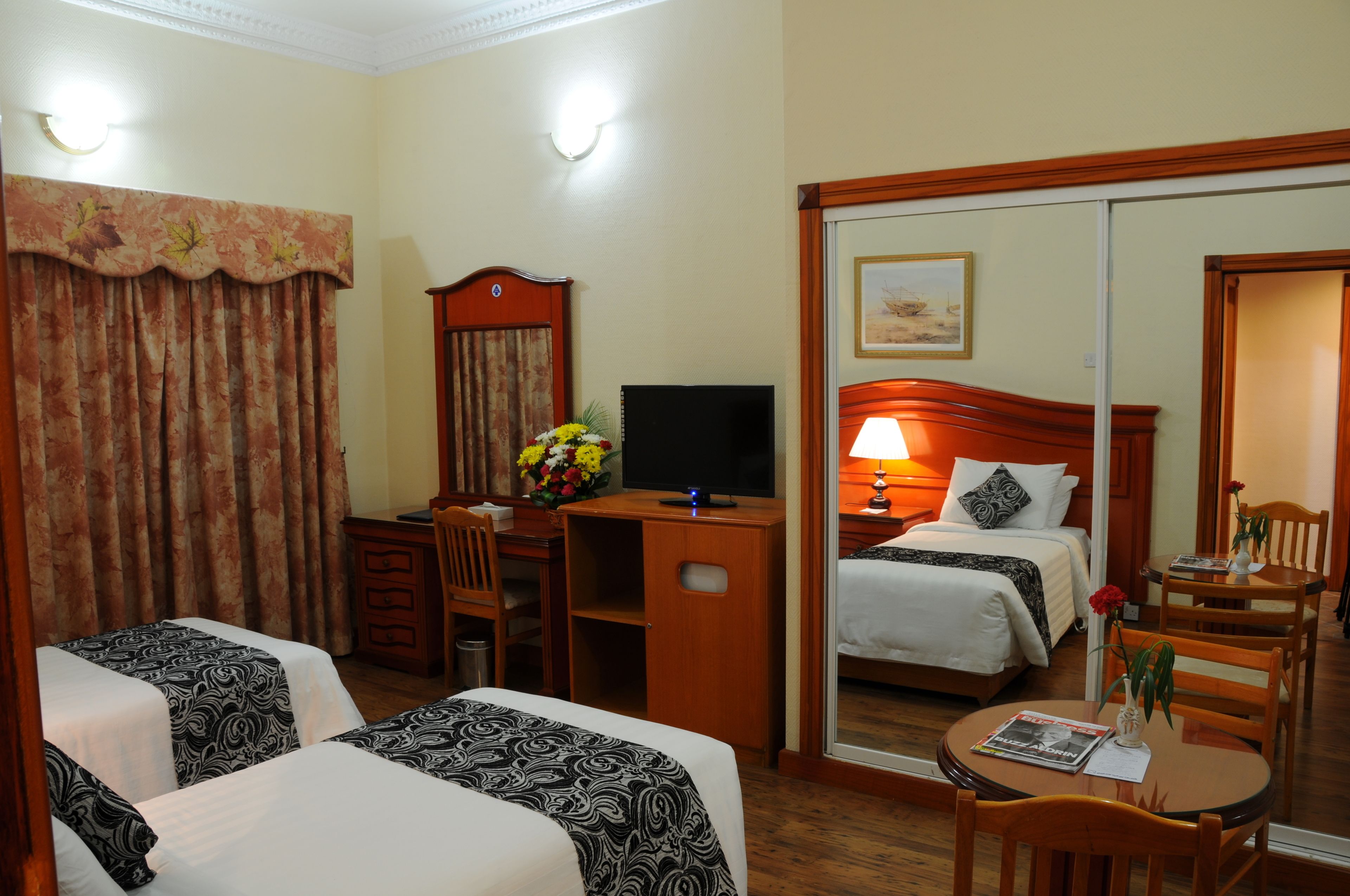 Een hotelkamer met twee bedden, een bureau met een computer, een stoel, een klein tafeltje met een vaas en een spiegel.