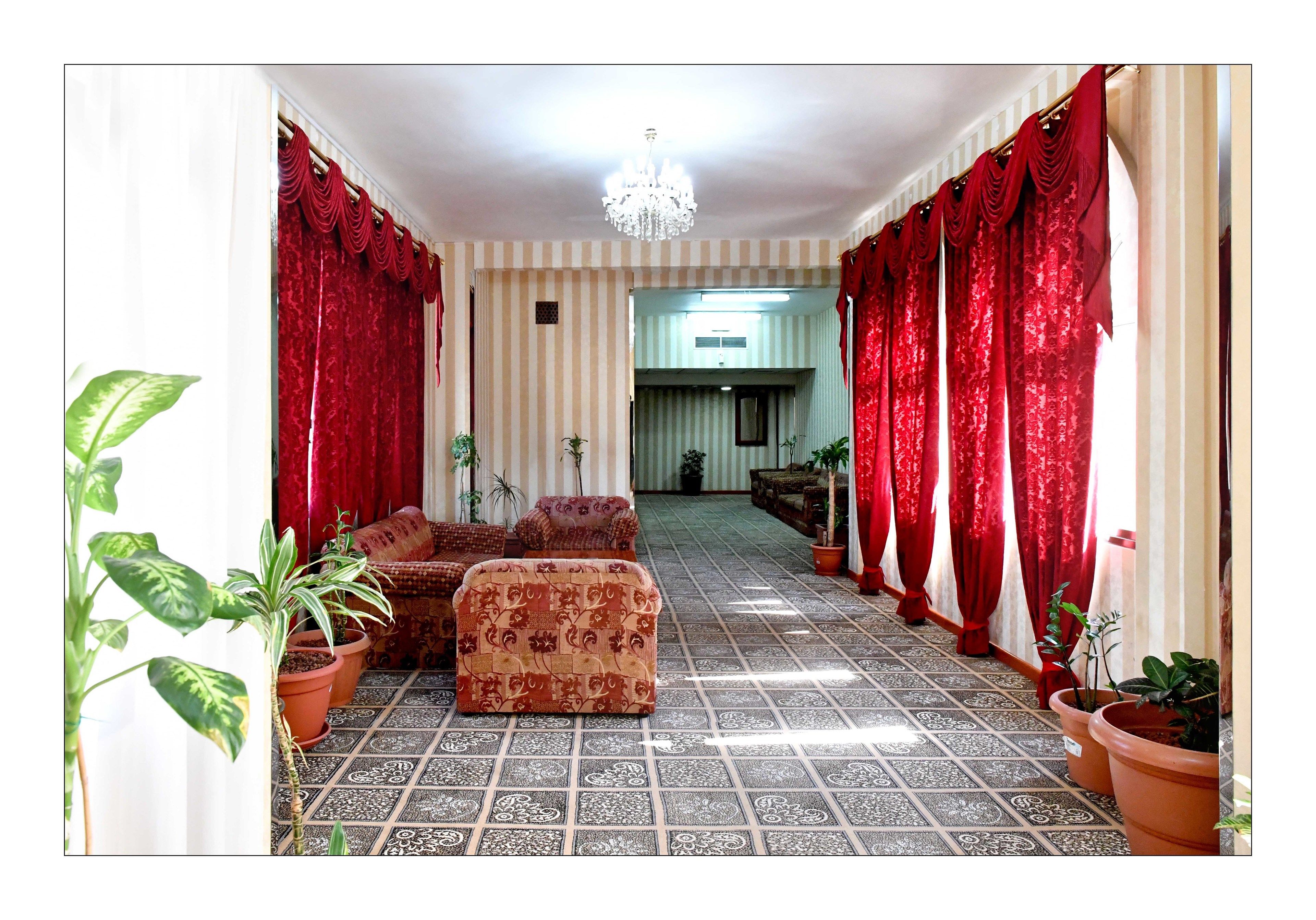 A hallway with patterned flooring, red curtains, and potted plants.