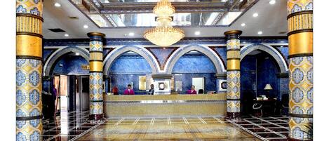 A lobby with ornate columns, a chandelier, and a reception desk.