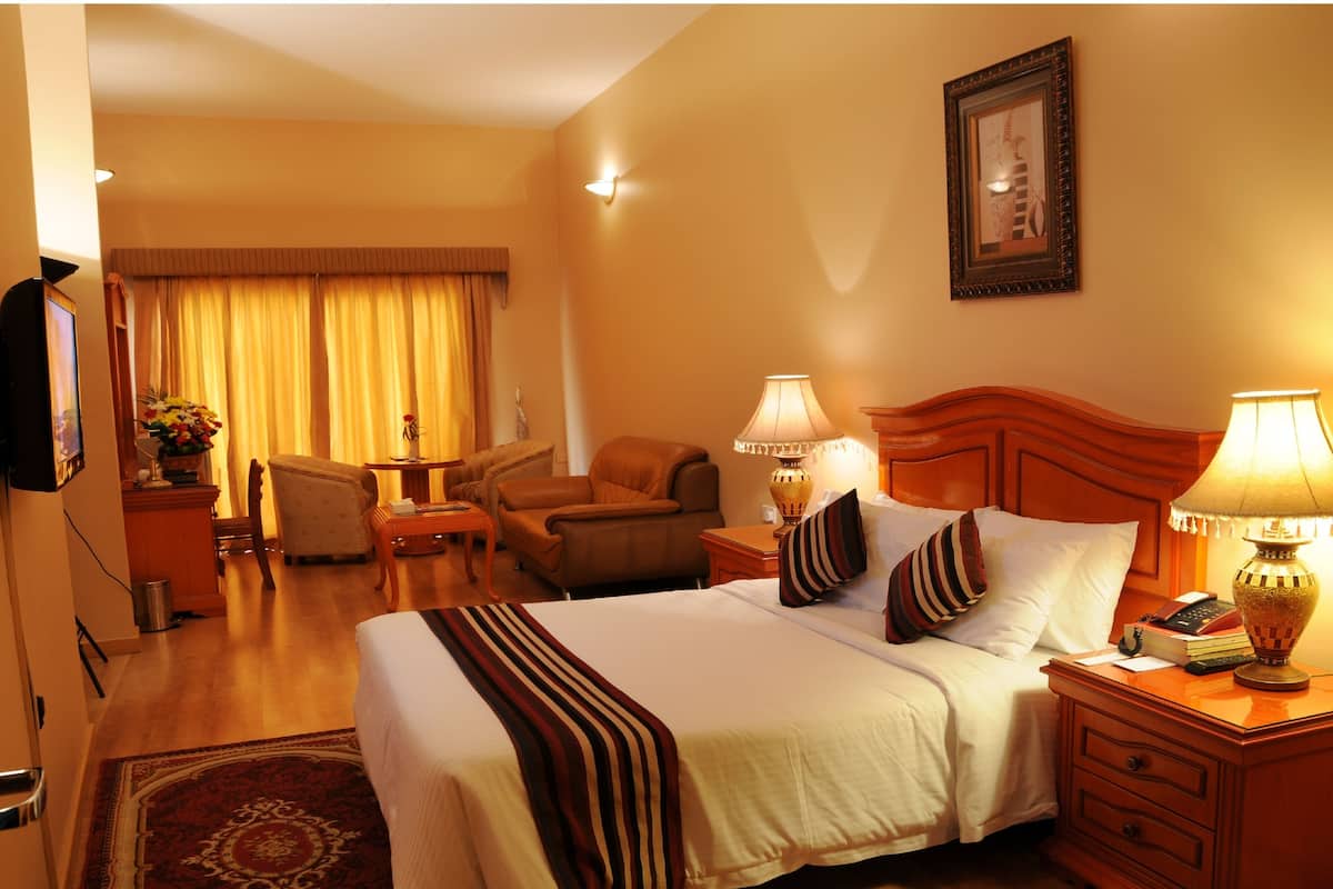 A hotel room with a large bed, two bedside lamps, a wooden nightstand, a chair, a small table with a vase of flowers, and a framed picture on the wall.