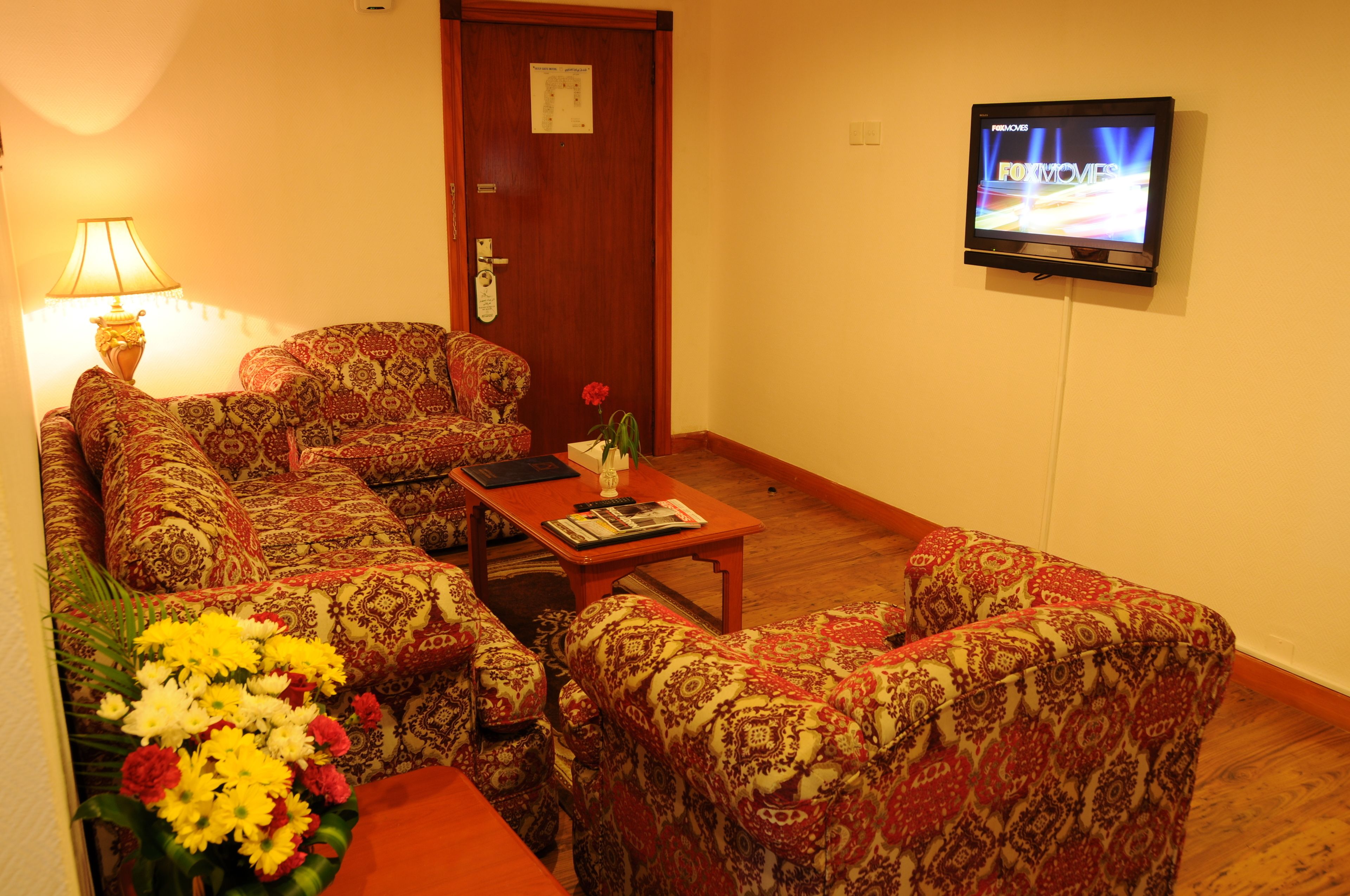 Ein Wohnzimmer mit gemusterten Sofas, einem Couchtisch, einem an der Wand montierten Fernseher und einer Tür mit einem Schild.