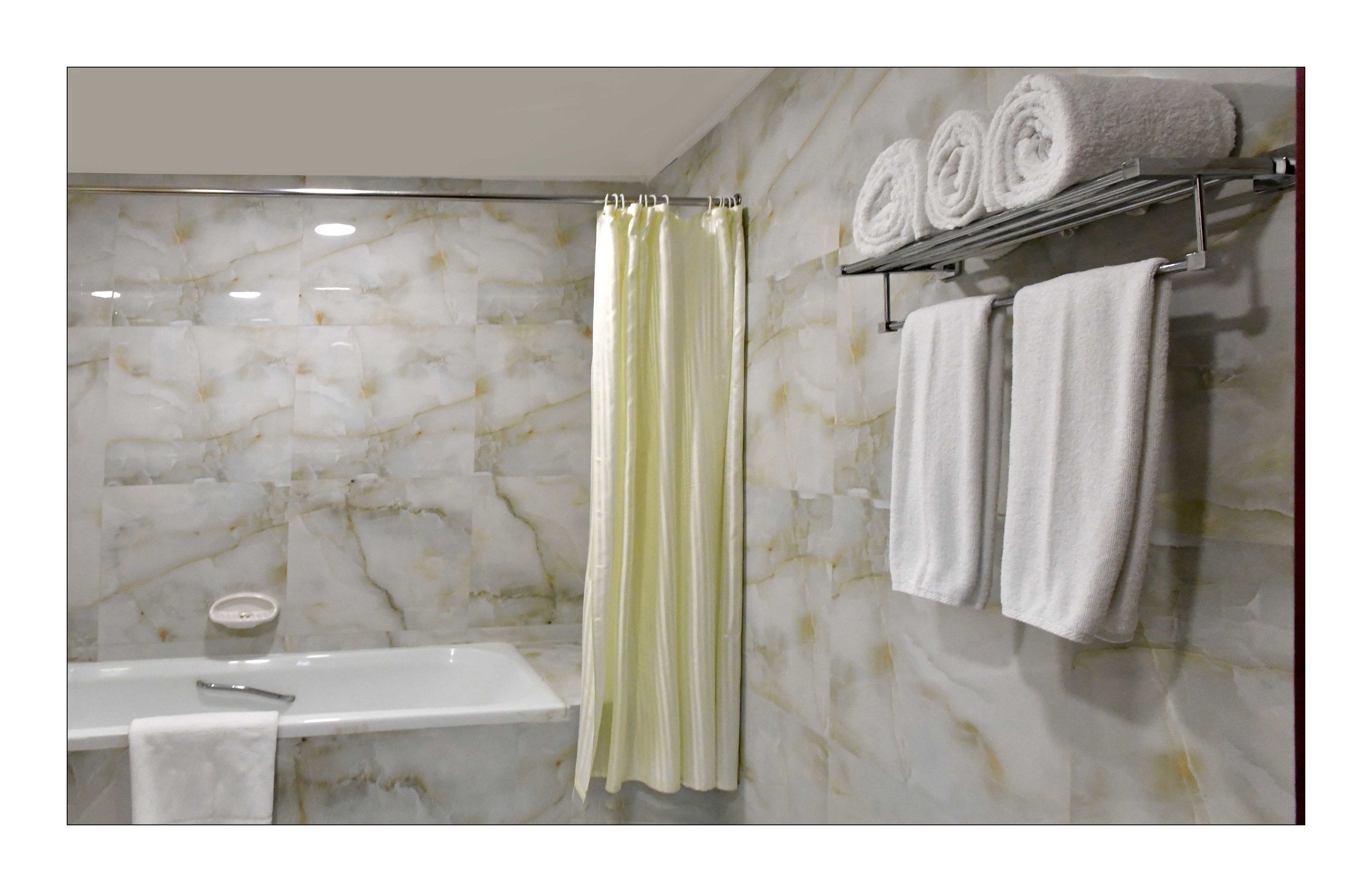 Une salle de bain avec un mur en marbre, un rideau de douche, un porte-serviettes avec des serviettes et une baignoire.