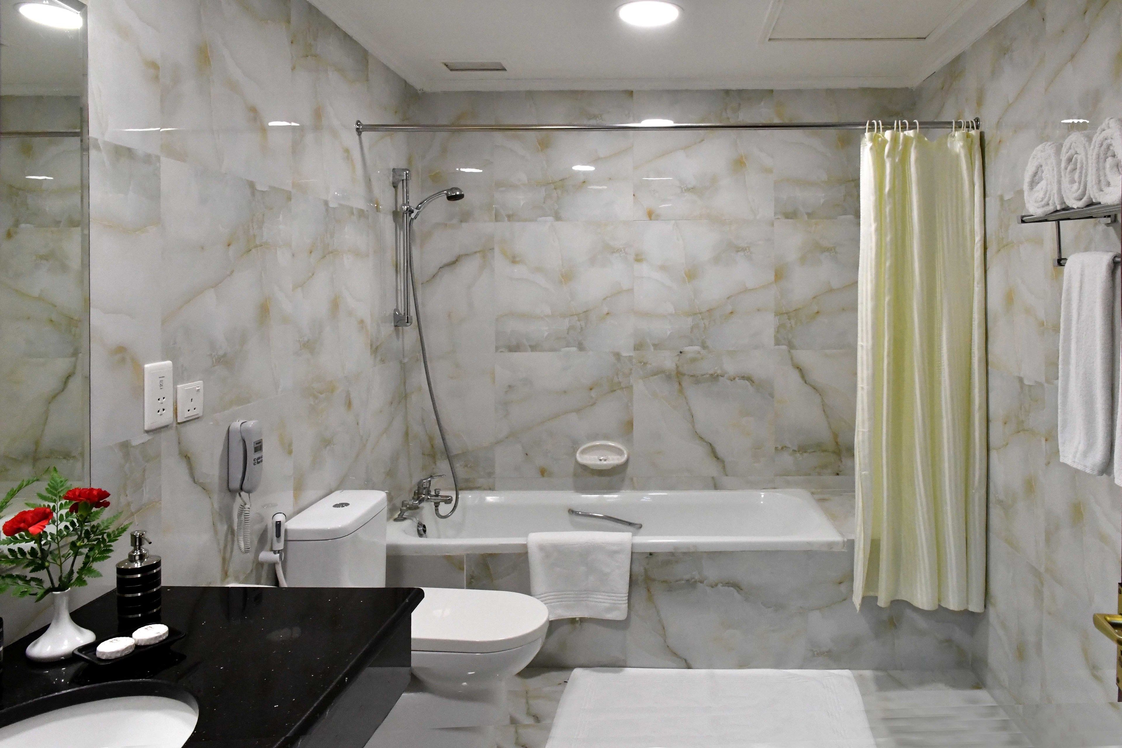 A bathroom with a marble wall, a bathtub, a toilet, a sink, and a shower.
