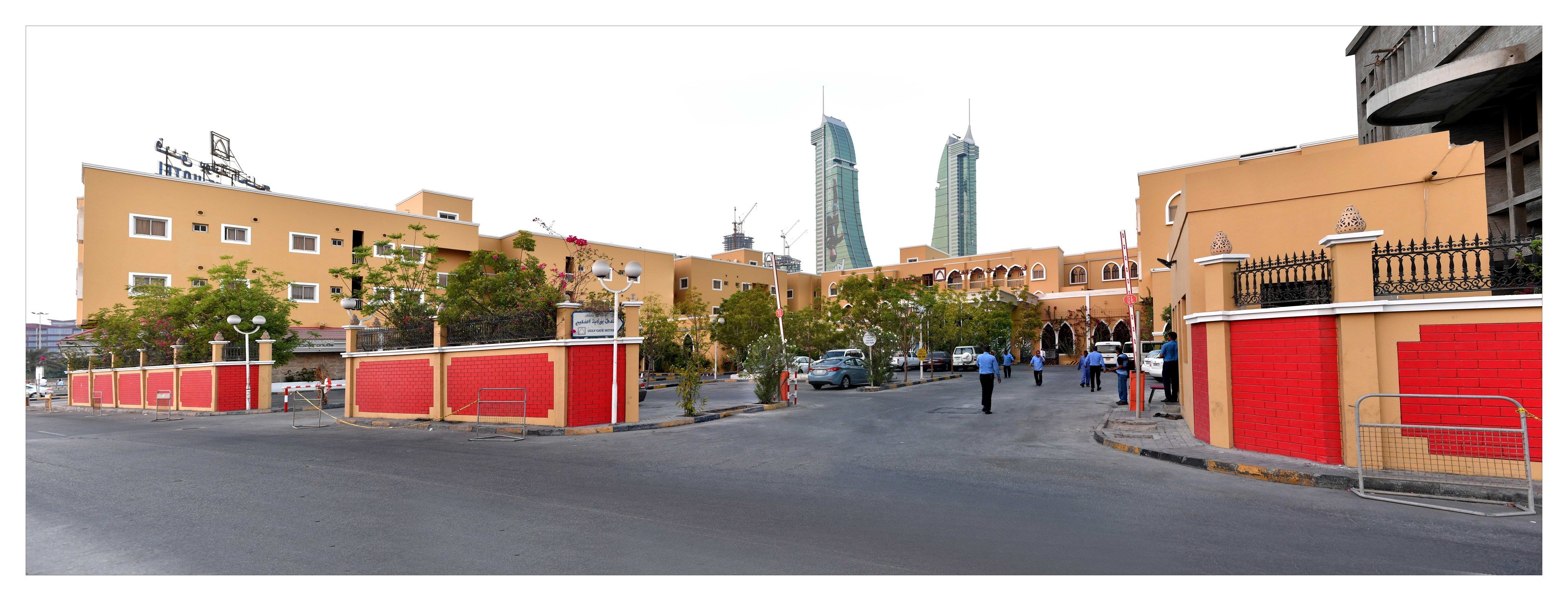 A street with buildings, a red gate, and a few people walking.