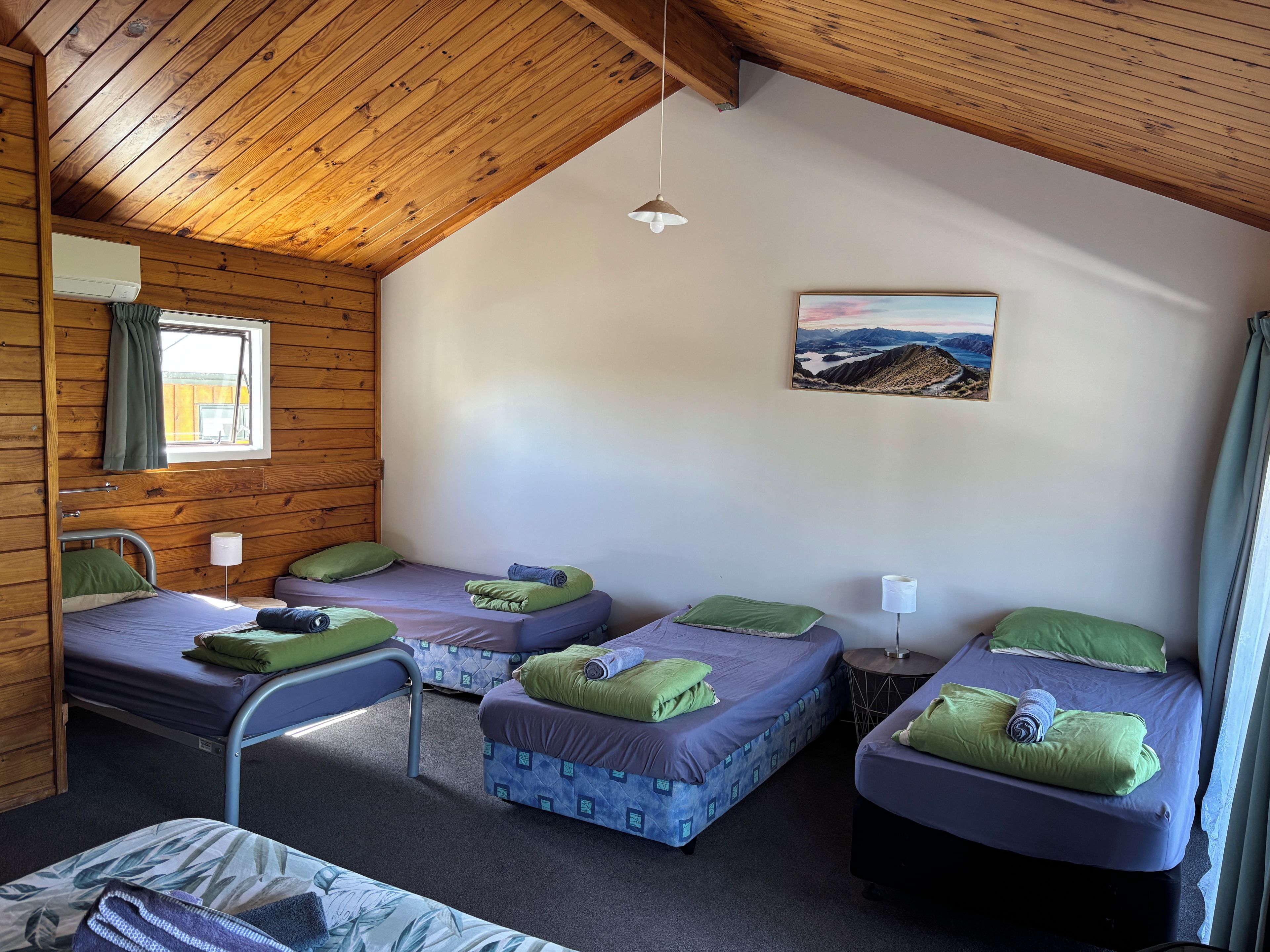 A cabin with four beds, a window with curtains, a painting on the wall, and a ceiling fan.