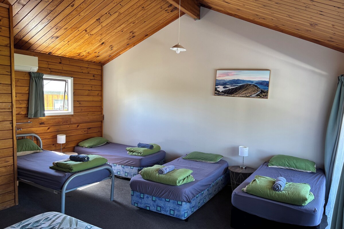 A cabin with four beds, a window with curtains, a painting on the wall, and a ceiling fan.