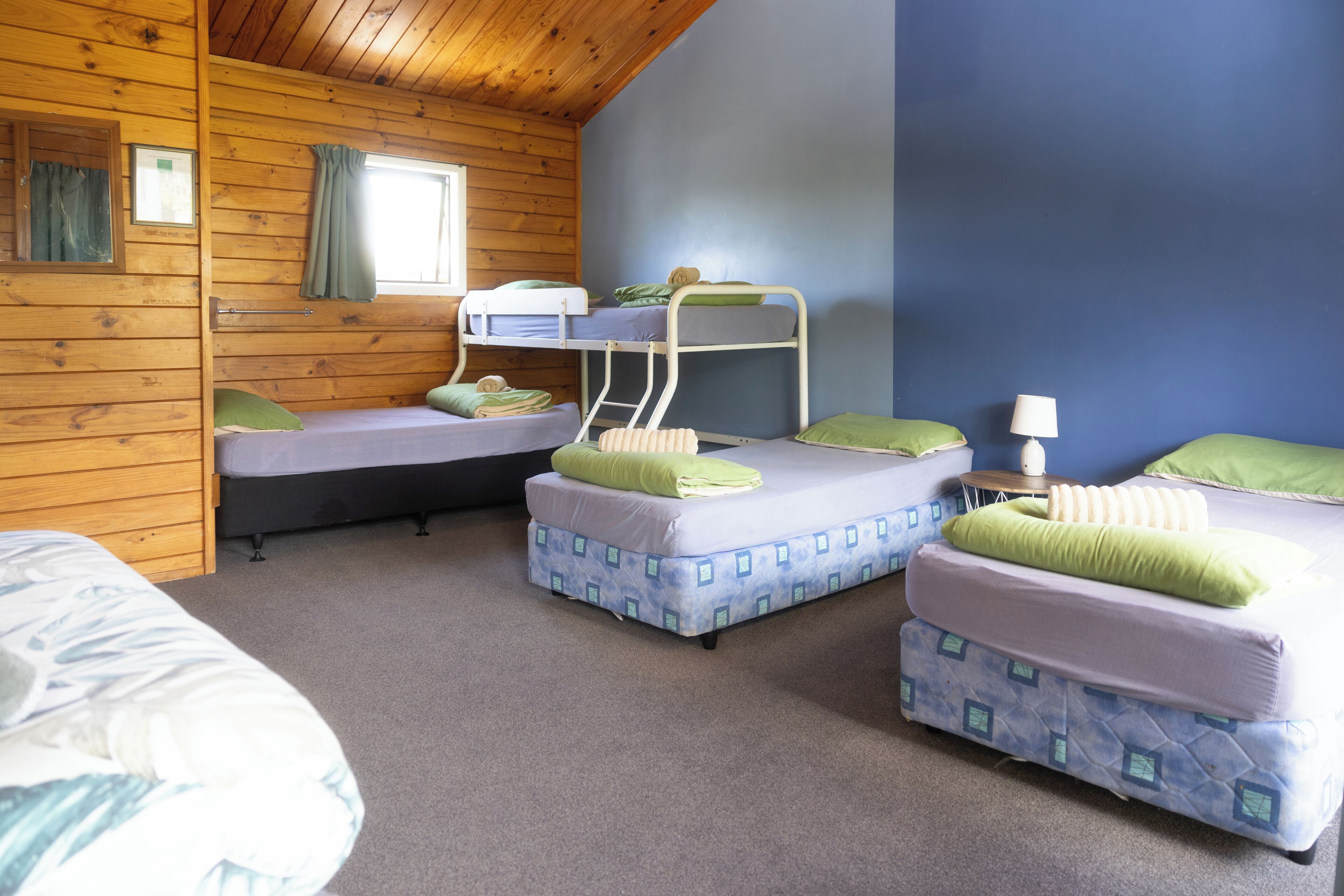 A room with bunk beds, a window with curtains, a lamp, and a bed with a patterned cover.