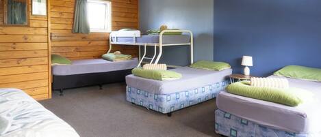A room with bunk beds, a window with curtains, a lamp, and a bed with a patterned cover.