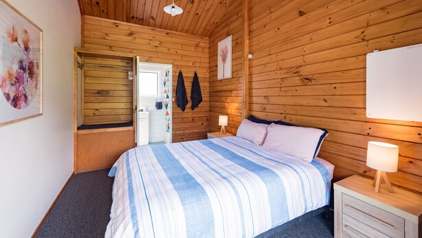 A wooden-paneled bedroom with a bed, bedside tables, and a door leading to another room.