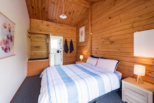 Dormitorio con paneles de madera, una cama, mesitas de noche y una puerta que da a otra habitación.