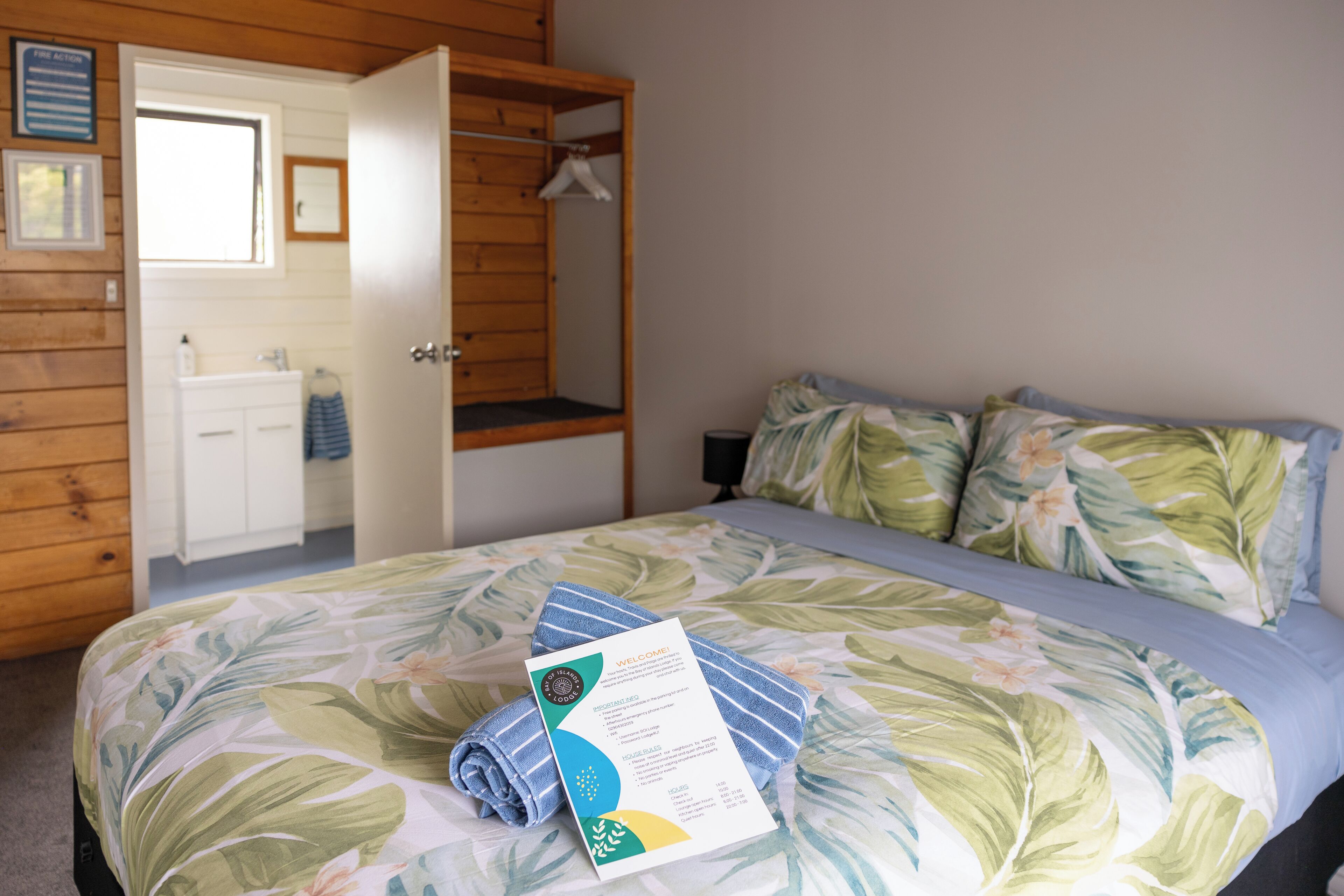 A hotel room with a bed, a wooden wardrobe, a bathroom, and a welcome brochure.