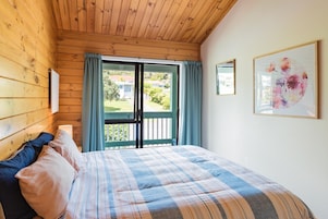 Un dormitorio con techo de madera, una cama con colcha escocesa, una ventana con cortinas y una obra de arte floral enmarcada en la pared.