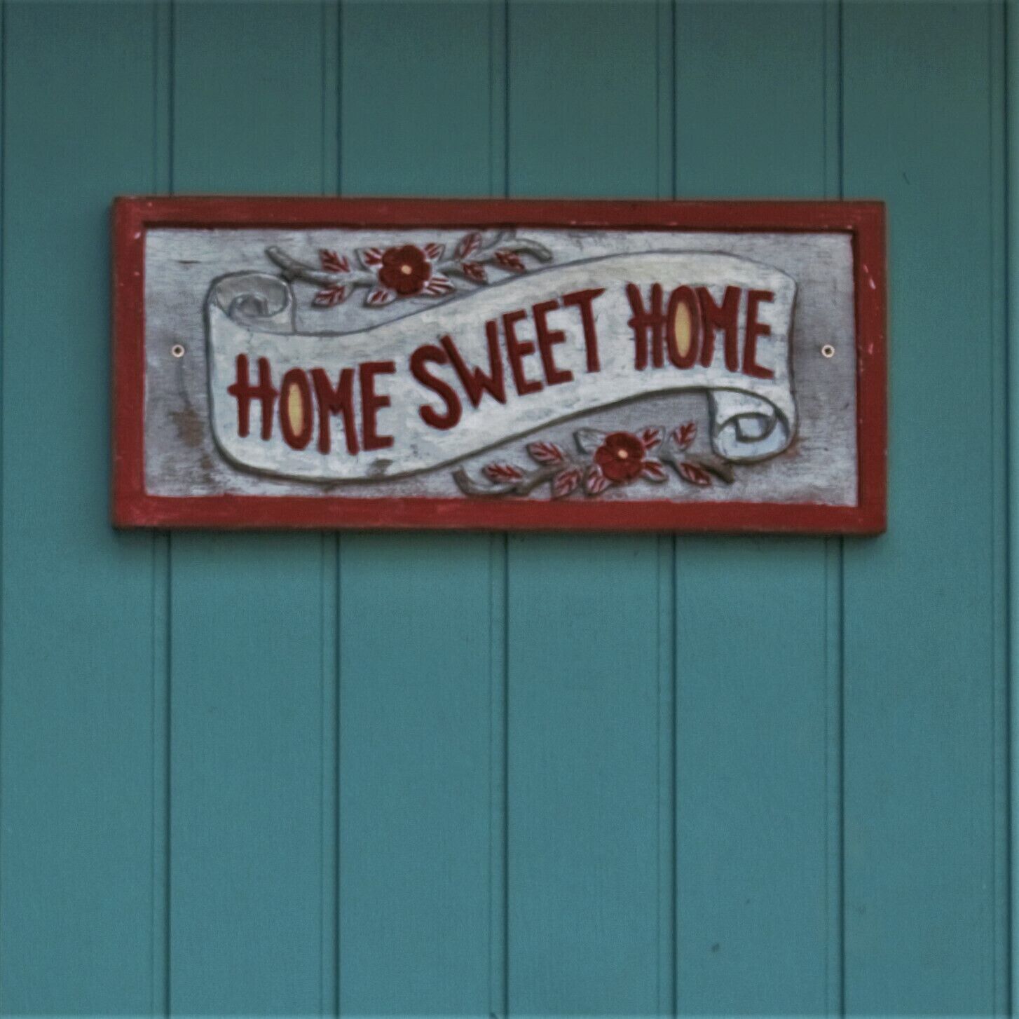 Un cartel con el texto 'HOME SWEET HOME' sobre un fondo verde azulado.