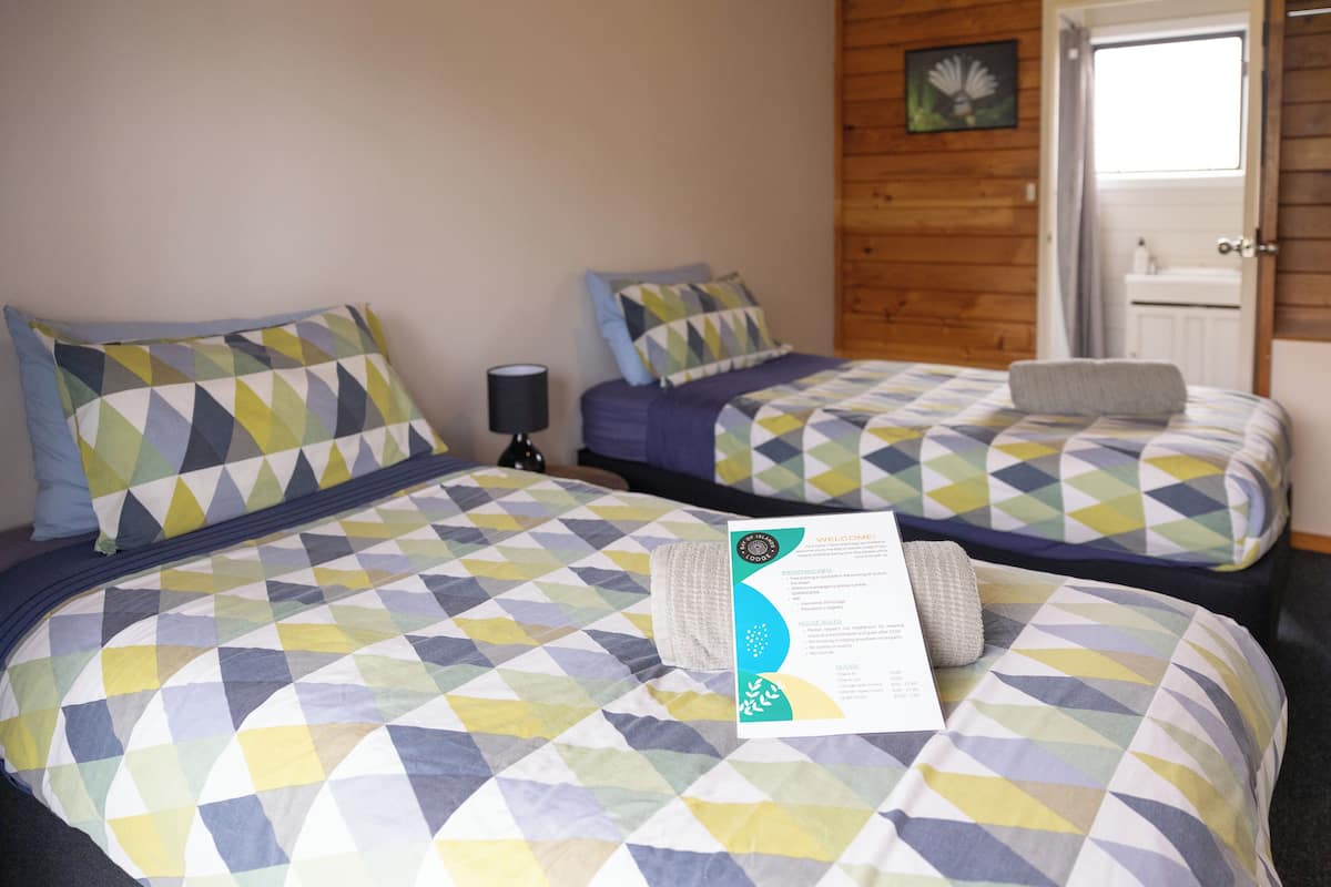 Zwei Betten mit geometrischen Musterbezügen, eine Nachttischlampe und eine Willkommenskarte auf dem Bett links.