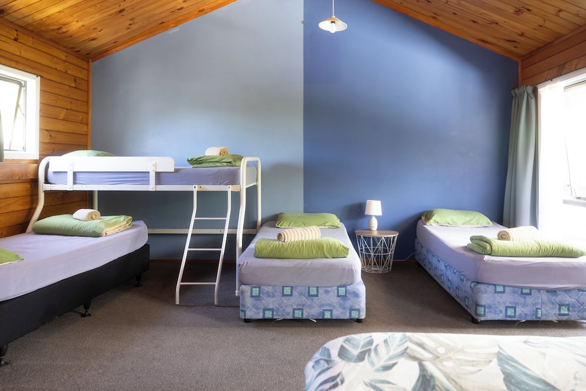 Ein Zimmer mit Etagenbetten, einer Stehleiter, einer Lampe und einem Fenster.
