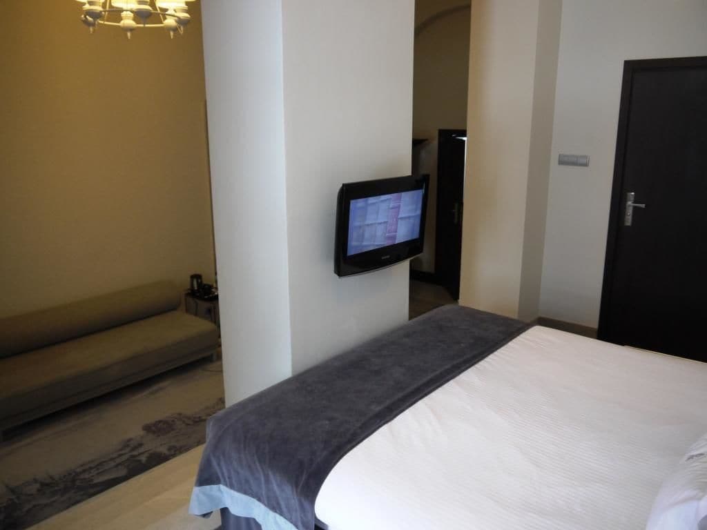 A hotel room with a bed, a television mounted on the wall, a sofa, and a door.